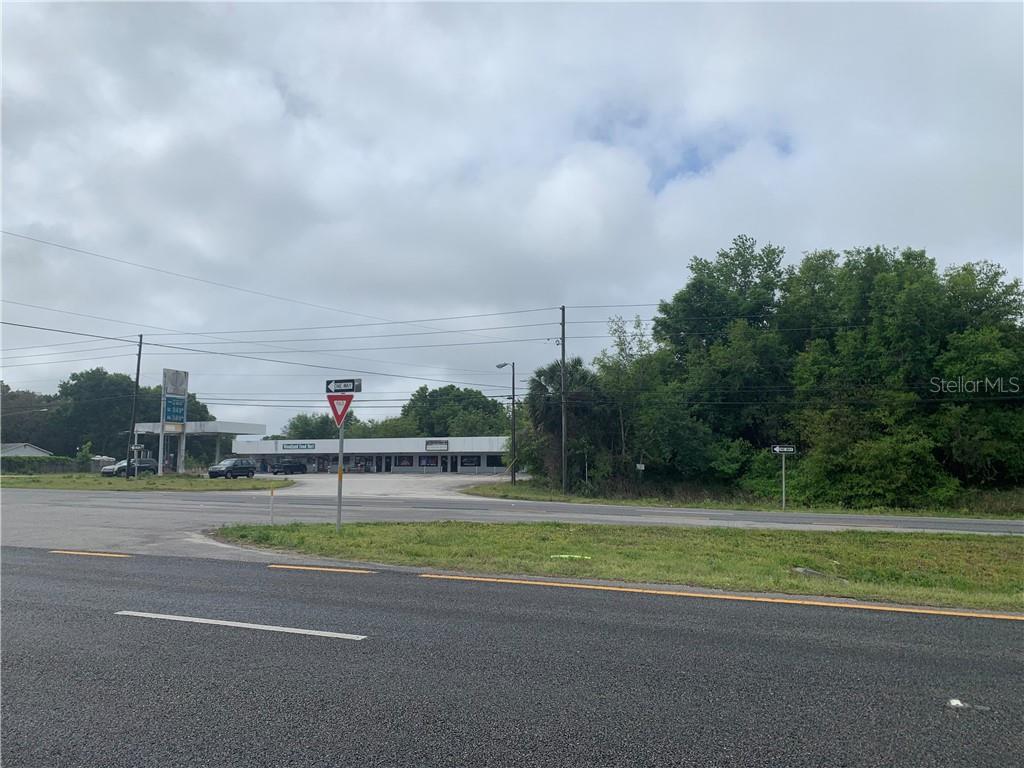 A commercial building with a gas station canopy sits across a road from a grassy area — 0 N WOODLAND BOULEVARD, DELAND, FL