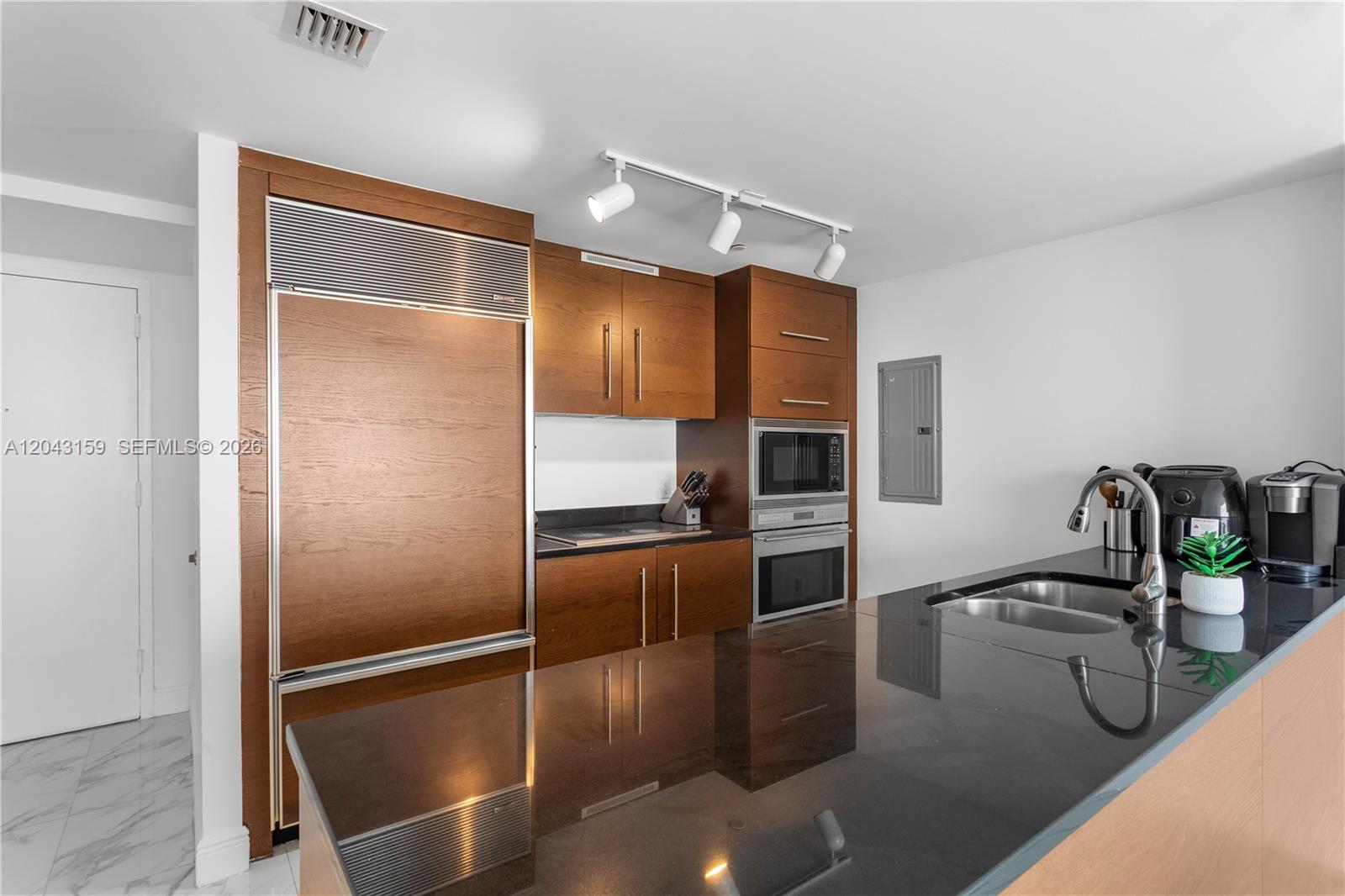 A modern kitchen features wood-paneled cabinetry, black countertops, and stainless steel appliances — 465 Brickell Ave # 5505, Miami FL 33131, MIAMI, FL