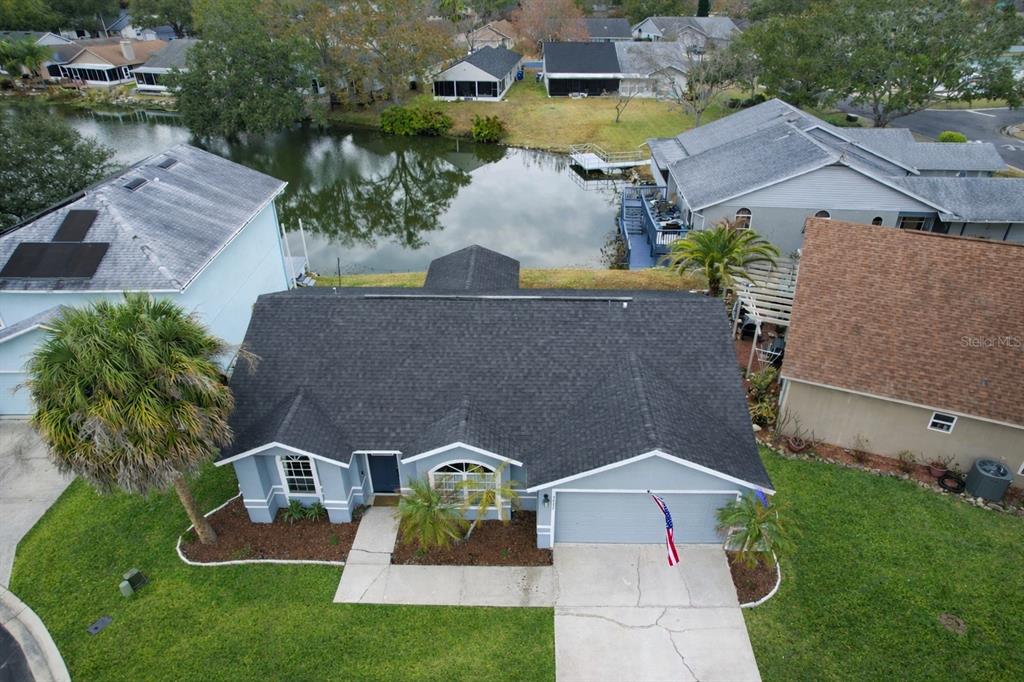An aerial view shows a single-story house with a dark roof and a backyard pond — 2022 HATTERAS POINT, LAKELAND, FL