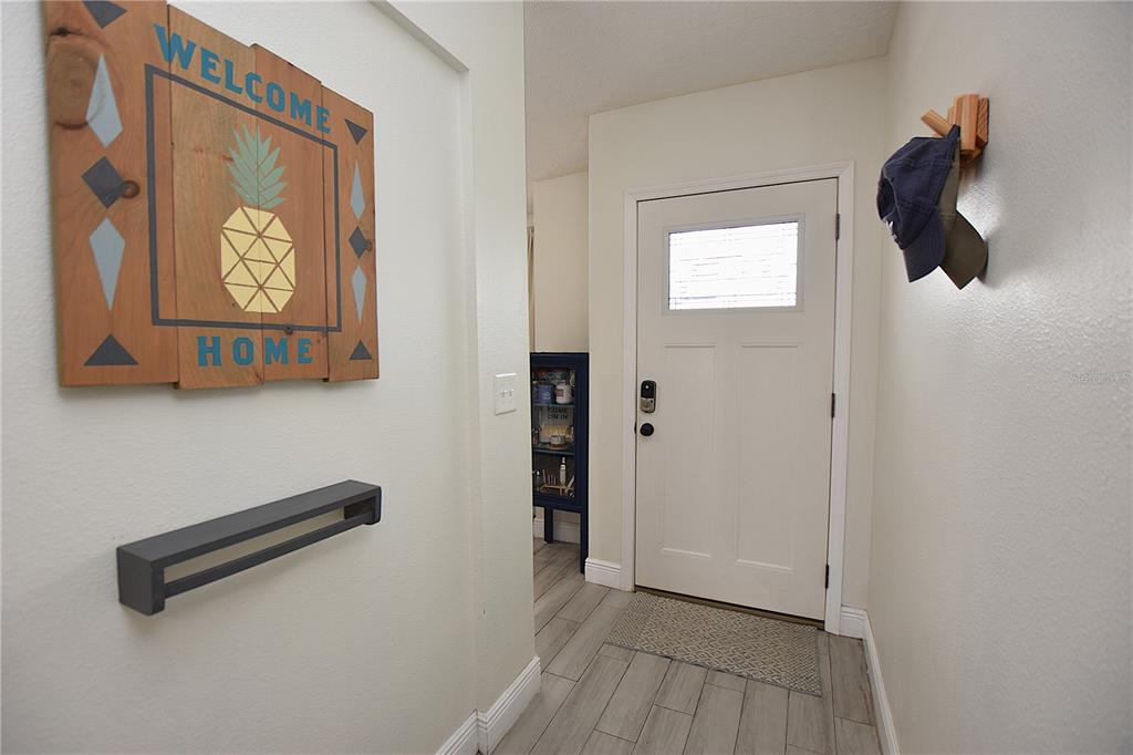 An entryway features a white door, wood-look tile flooring, a wall-mounted coat hook, and decor — 2022 HATTERAS POINT, LAKELAND, FL