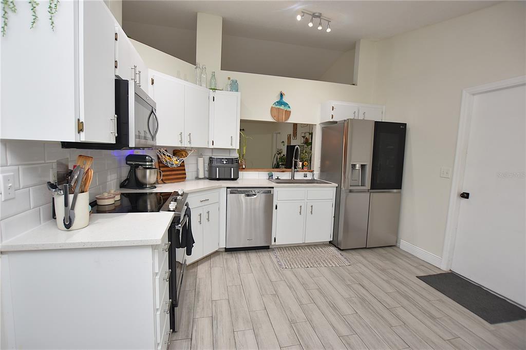 A kitchen features white cabinets, stainless steel appliances, a subway tile backsplash, and light flooring — 2022 HATTERAS POINT, LAKELAND, FL