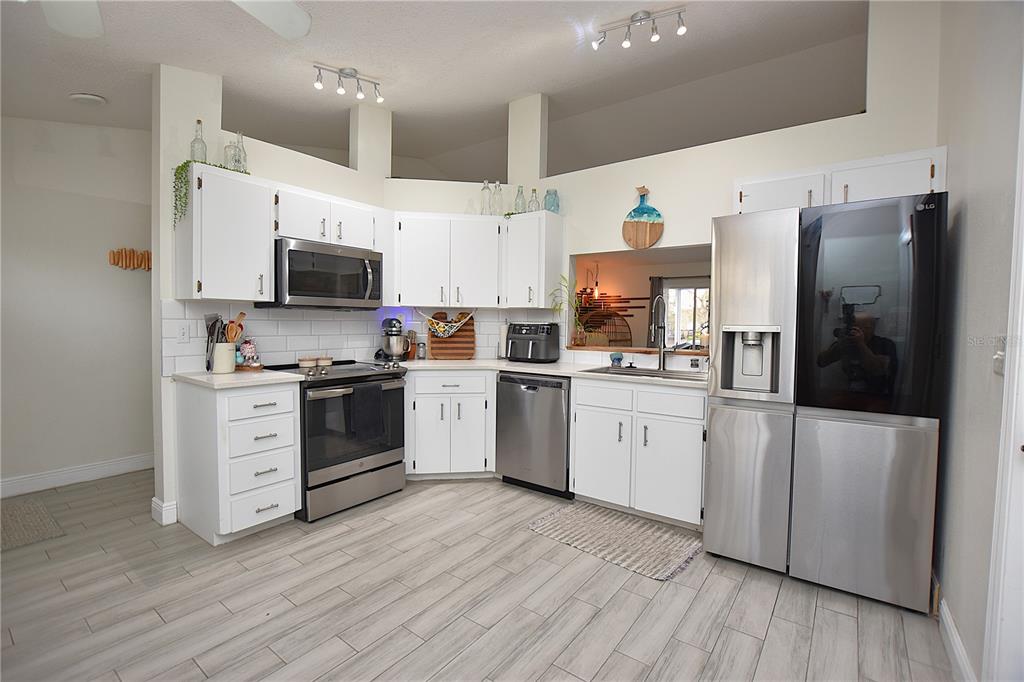 A kitchen features white cabinets, stainless steel appliances, a subway tile backsplash, and wood-look flooring — 2022 HATTERAS POINT, LAKELAND, FL