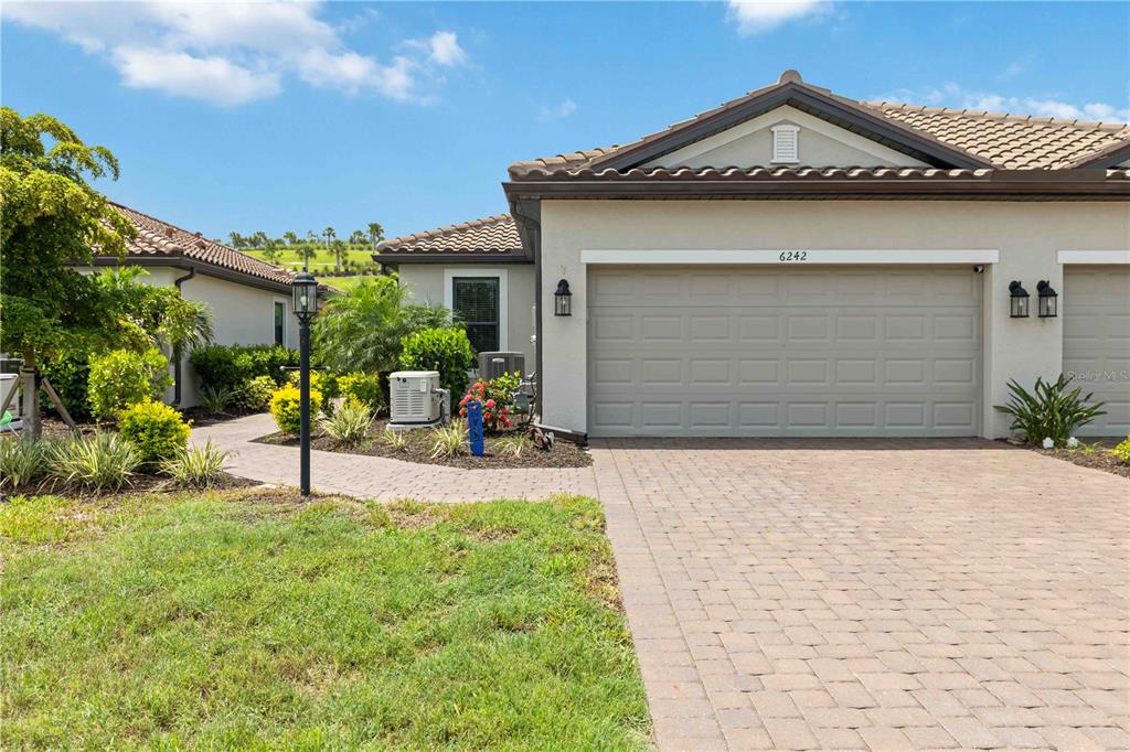 A single-story house features a beige stucco exterior, a tiled roof, and a paved driveway — 6242 GRANDVIEW HILL COURT, BRADENTON, FL