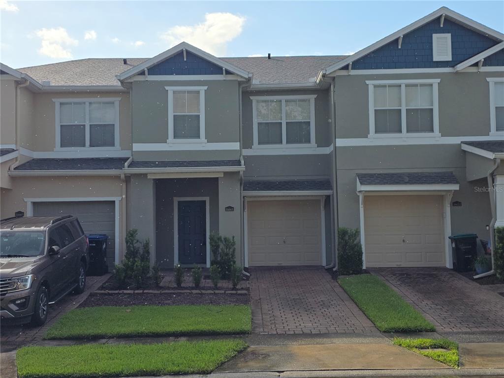 A row of three two-story townhouses with beige stucco, gray siding, and attached garages — 16661 CEDAR CREST DRIVE, ORLANDO, FL