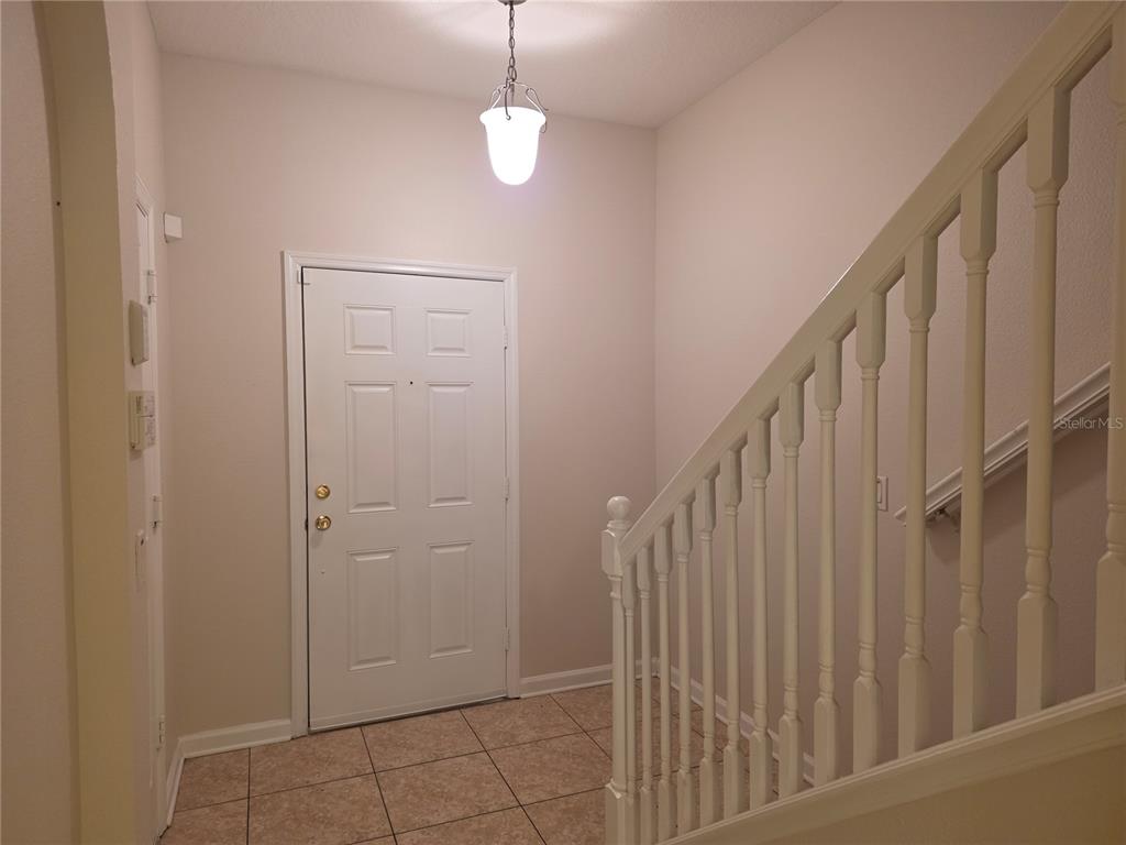 An entryway features a white door, tiled floor, and a staircase with a white railing — 16661 CEDAR CREST DRIVE, ORLANDO, FL