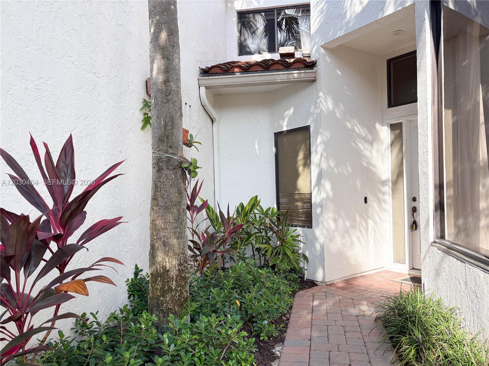 A brick walkway leads to the front entrance of a white stucco home with landscaping — 2530 Windsor Way Ct, Wellington FL 33414, WELLINGTON, FL
