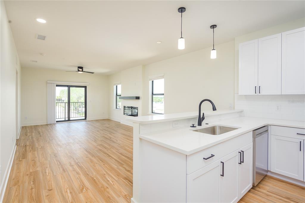 A kitchen with white cabinets and a sink overlooks an open living area with flooring — 419 SE 1ST AVENUE UNIT 201, OCALA, FL