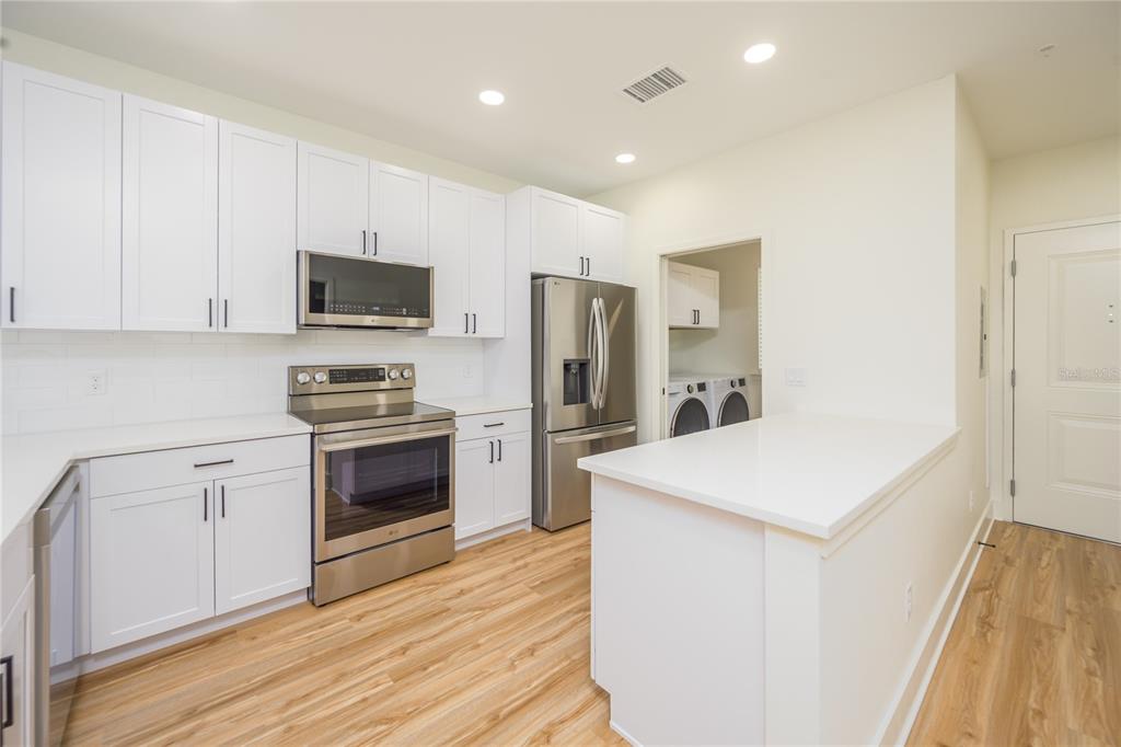 A modern kitchen features white cabinets, stainless steel appliances, and a white countertop island — 419 SE 1ST AVENUE UNIT 201, OCALA, FL