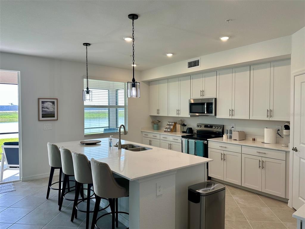 A modern kitchen features white cabinets, a large island with bar seating, and stainless appliances — 12680 RADIANCE COURT UNIT 102, VENICE, FL