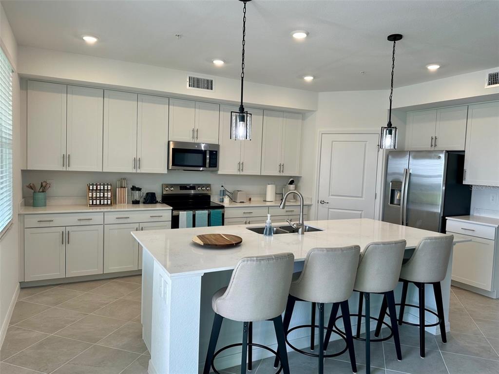 A modern kitchen features white cabinetry, a large quartz island with seating, and stainless appliances — 12680 RADIANCE COURT UNIT 102, VENICE, FL