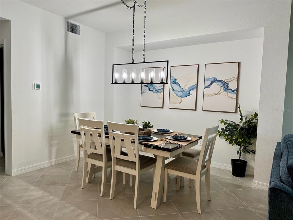 A dining room features a rectangular table with six chairs under a modern linear chandelier — 12680 RADIANCE COURT UNIT 102, VENICE, FL