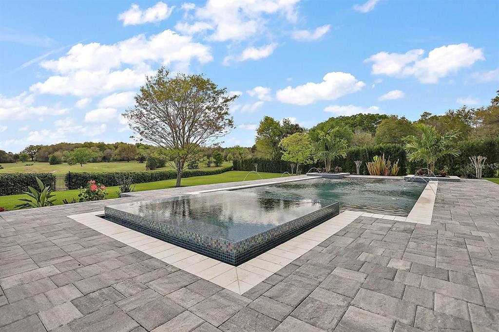 A rectangular infinity pool with tiled edges sits on a gray paver patio outdoors — 25868 CROSSINGS BLUFF LANE, SORRENTO, FL