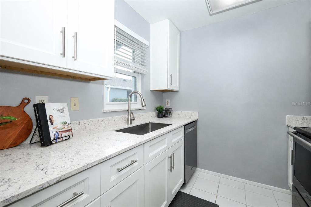 A kitchen features white cabinets, speckled countertops, a stainless steel sink, and light gray walls — 115 DORCHESTER SQUARE, LAKE MARY, FL