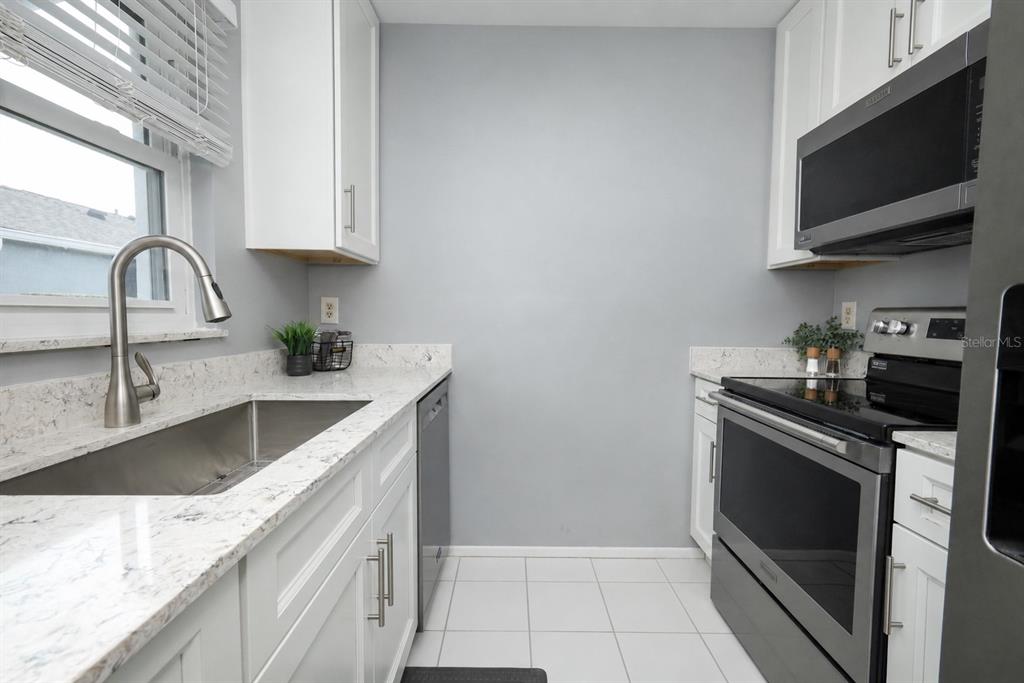 A galley kitchen features white cabinets, stainless steel appliances, and light-colored stone countertops — 115 DORCHESTER SQUARE, LAKE MARY, FL