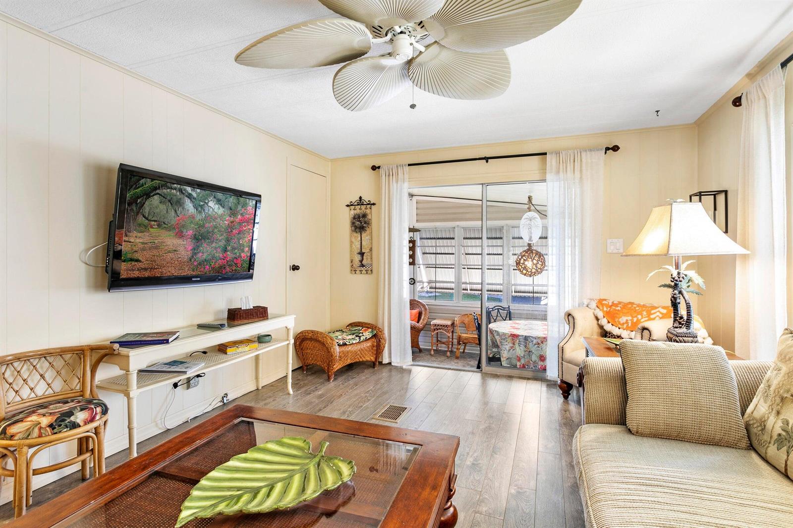 A living room features a ceiling fan, wood-look flooring, a wall-mounted television, and sliding doors — 37039 Exuma Bay, Boynton Beach FL 33436, BOYNTON BEACH, FL