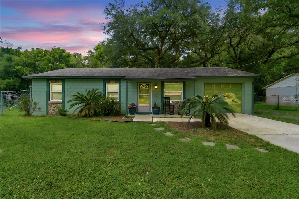 A single-story green house with a front lawn, attached garage, and large shade trees — 2120 TANGLEWOOD DRIVE, ORANGE CITY, FL
