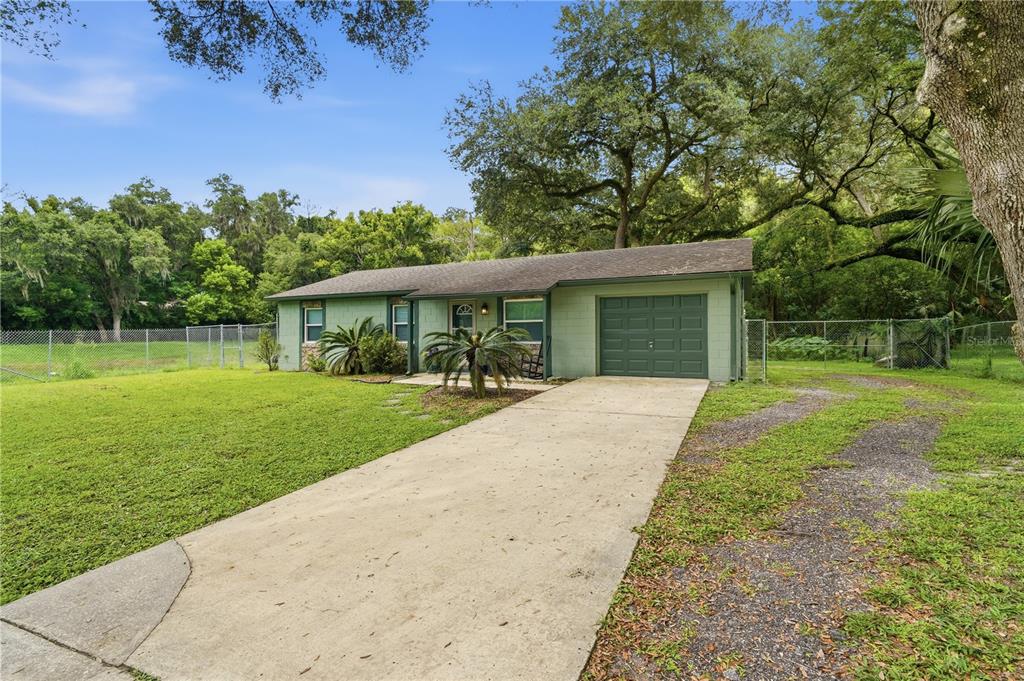 A single-story green house with a concrete driveway and a garage sits on a lawn — 2120 TANGLEWOOD DRIVE, ORANGE CITY, FL