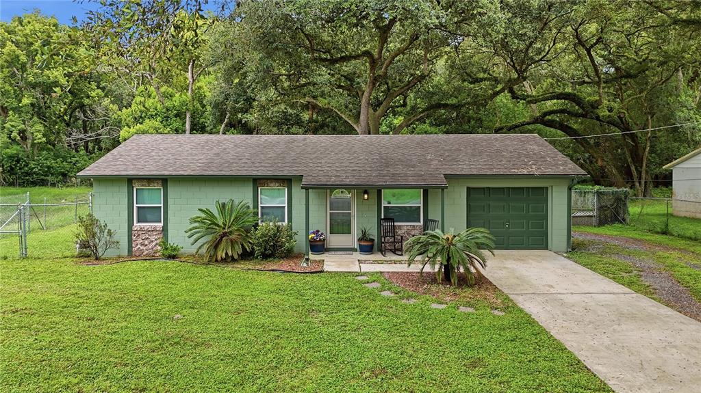 A single-story green house with a concrete driveway and a large front lawn — 2120 TANGLEWOOD DRIVE, ORANGE CITY, FL