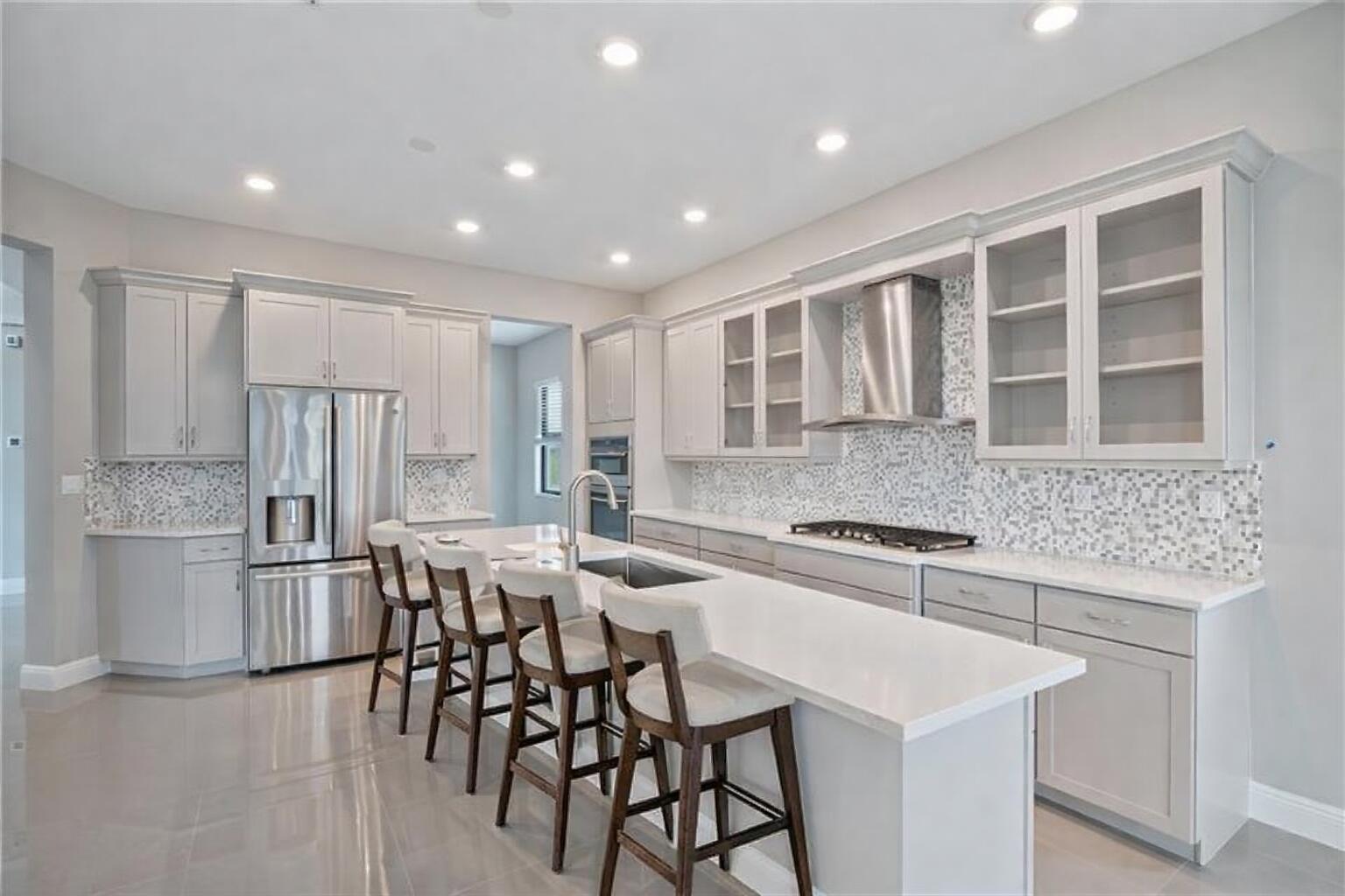 A modern kitchen features light gray cabinetry, stainless steel appliances, and a white quartz island — 12175 N Baypoint Circle, Parkland FL 33076, PARKLAND, FL