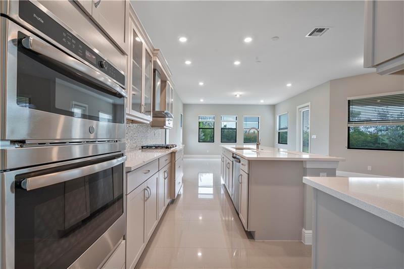 A modern kitchen features light gray cabinetry, stainless steel appliances, and a large center island — 12175 N Baypoint Circle, Parkland FL 33076, PARKLAND, FL