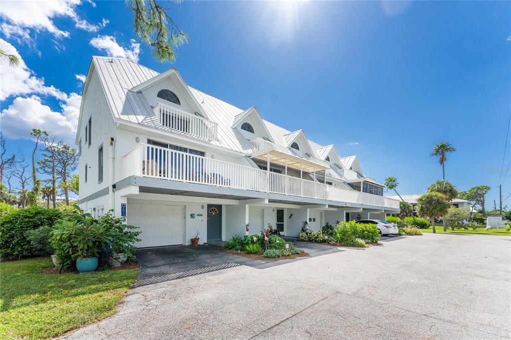 A multi-story white townhouse building with a metal roof, balconies, and ground-level garages — 6800 PLACIDA ROAD UNIT TH2, 1B, ENGLEWOOD, FL