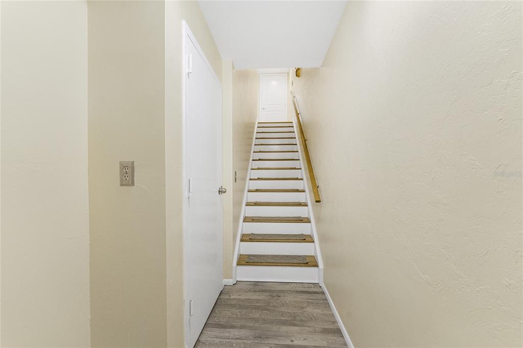 A staircase with wooden treads and a white handrail leads to a closed door upstairs — 6800 PLACIDA ROAD UNIT TH2, 1B, ENGLEWOOD, FL