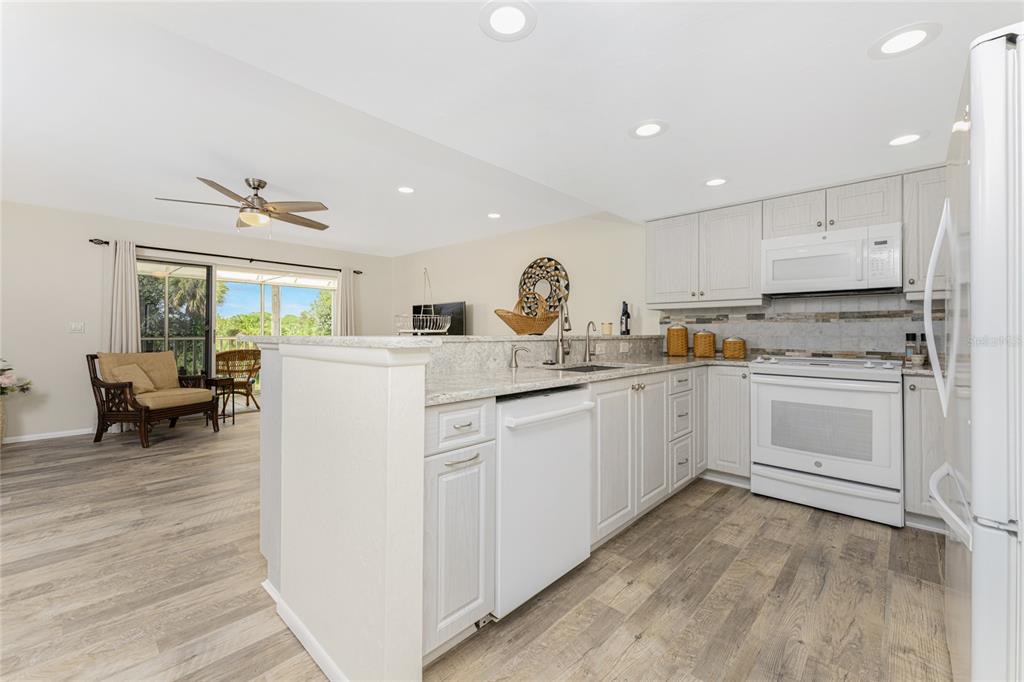 A kitchen with light wood cabinets, white appliances, and granite countertops opens to a living area — 6800 PLACIDA ROAD UNIT TH2, 1B, ENGLEWOOD, FL