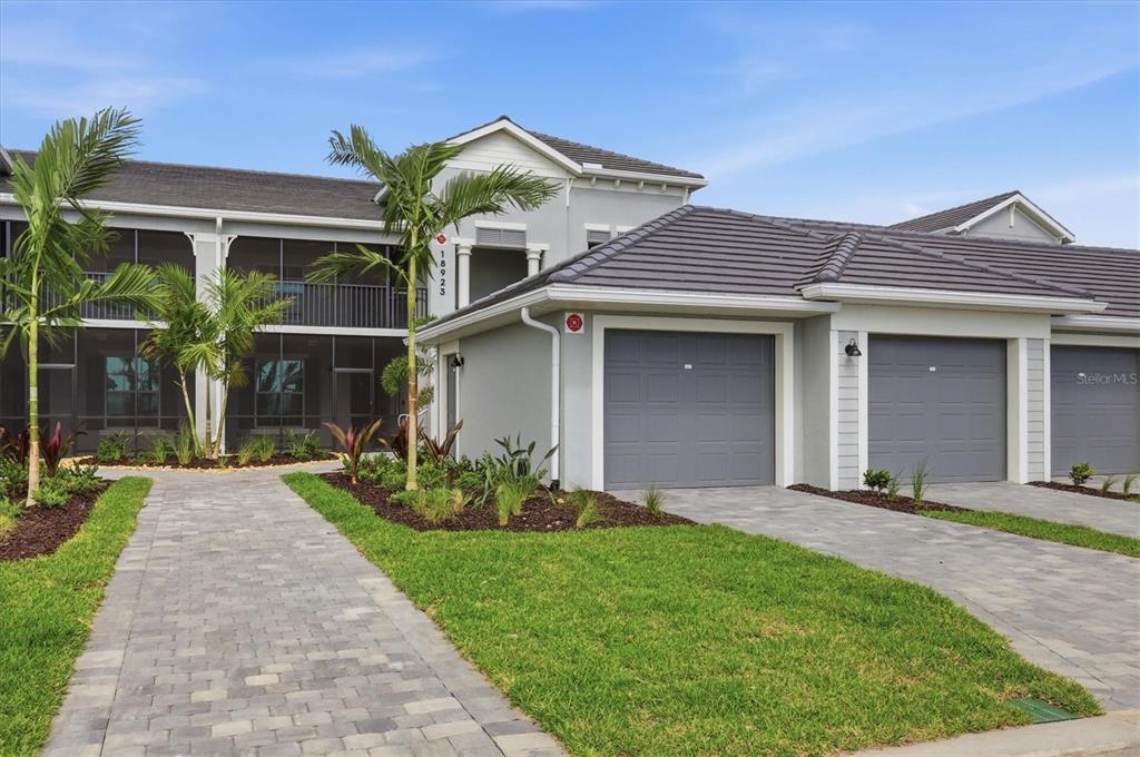A two-story building features a gray exterior, a paved walkway, and attached garages — 18923 SCALLOP LOOP UNIT 205, BRADENTON, FL