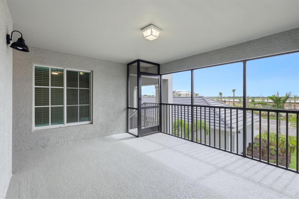 A covered balcony with a screened enclosure, textured walls, and a view of neighboring homes — 18923 SCALLOP LOOP UNIT 205, BRADENTON, FL