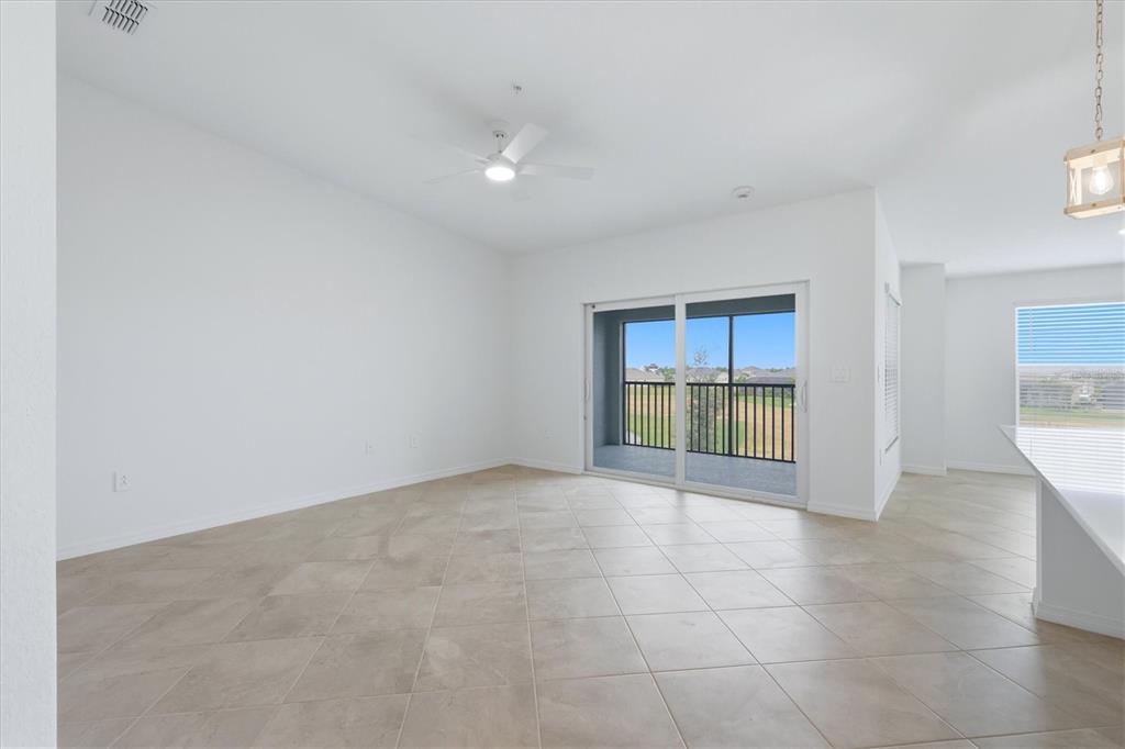 An empty living room with white walls, tile flooring, a ceiling fan, and sliding glass doors — 18923 SCALLOP LOOP UNIT 205, BRADENTON, FL