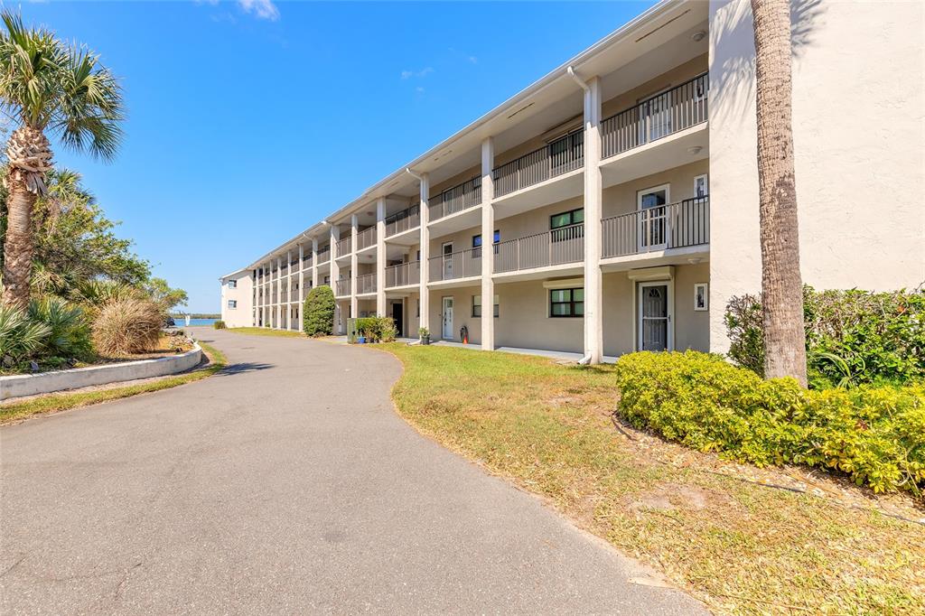 A multi-story apartment building with exterior balconies and a paved driveway under a blue sky — 2100 N PENINSULA AVENUE UNIT 1050, NEW SMYRNA BEACH, FL