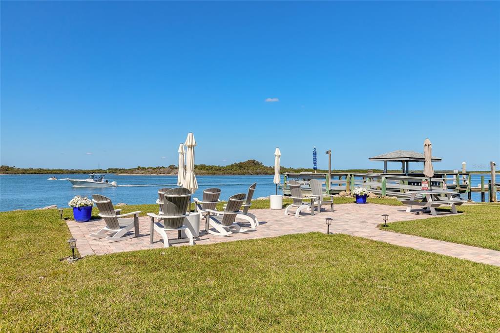 A paved patio with outdoor chairs overlooks a waterfront area with a boat and dock — 2100 N PENINSULA AVENUE UNIT 1050, NEW SMYRNA BEACH, FL