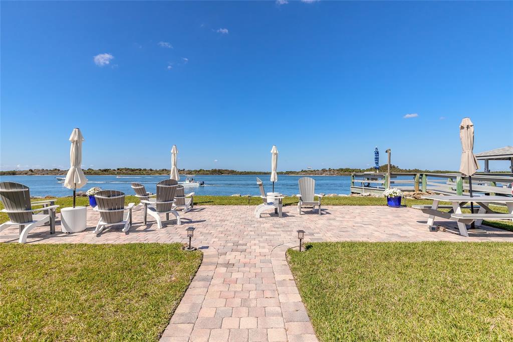 A paved patio with outdoor seating overlooks a body of water under a clear sky — 2100 N PENINSULA AVENUE UNIT 1050, NEW SMYRNA BEACH, FL