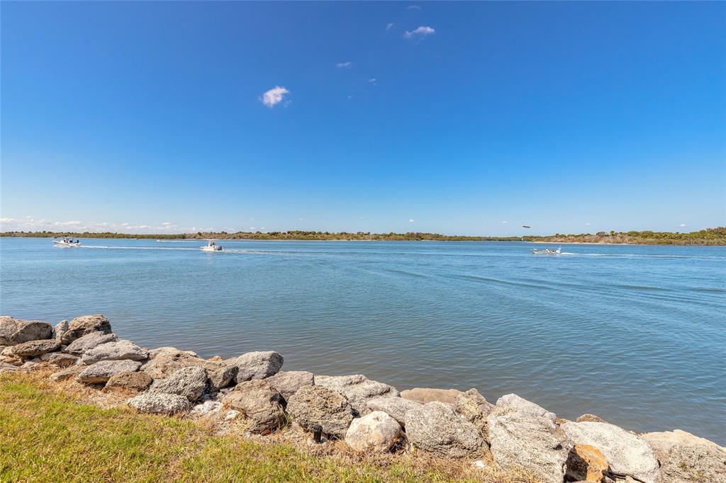 A rocky shoreline borders a wide waterway with several small boats under a clear sky — 2100 N PENINSULA AVENUE UNIT 1050, NEW SMYRNA BEACH, FL