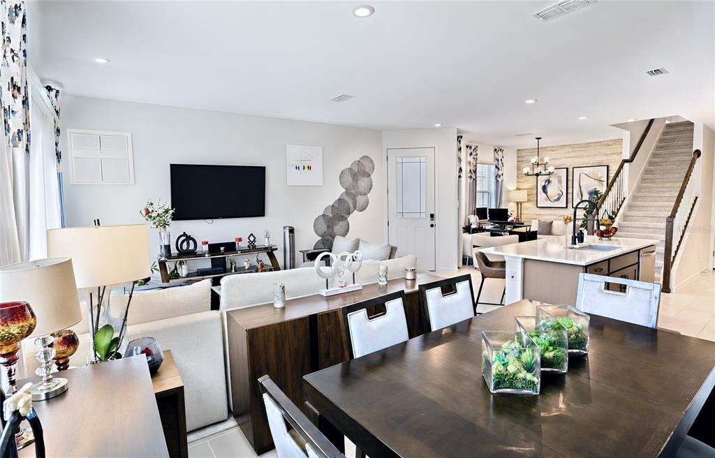 An open-concept living and dining area features a kitchen island, staircase, and neutral decor — 1120 LAKESHORE BREEZE PLACE, KISSIMMEE, FL