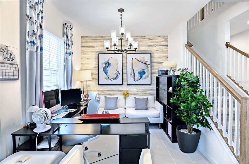A home office features a desk, white sofa, wood-look accent wall, and a staircase — 1120 LAKESHORE BREEZE PLACE, KISSIMMEE, FL
