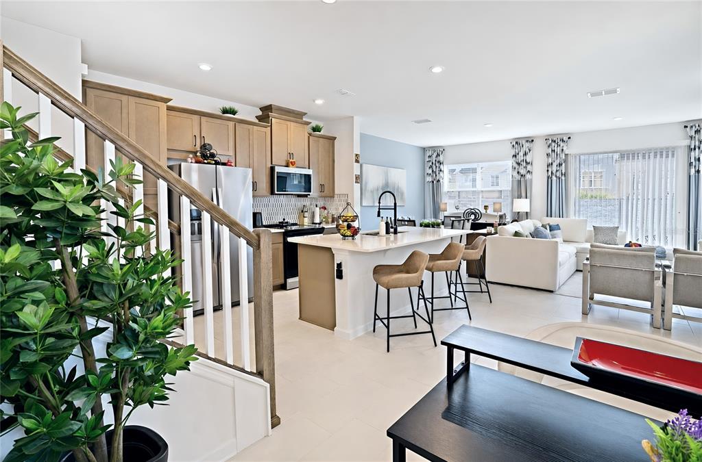 An open-concept kitchen and living area features light wood cabinets, a central island, and stairs — 1120 LAKESHORE BREEZE PLACE, KISSIMMEE, FL