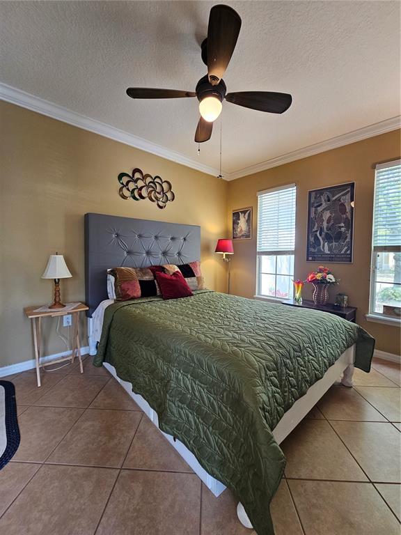 A bedroom features a tufted gray headboard, olive green quilt, tile flooring, and ceiling fan — 25147 IRONWEDGE DRIVE, SORRENTO, FL