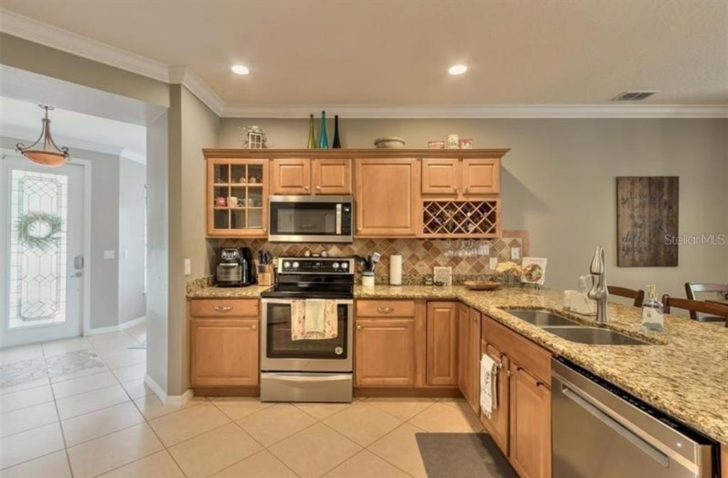 A kitchen with light wood cabinets, granite countertops, stainless steel appliances, and tile flooring — 25147 IRONWEDGE DRIVE, SORRENTO, FL
