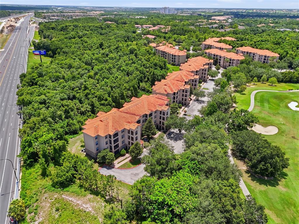 An aerial view shows multi-story apartment buildings situated between a highway and a golf course — 8020 TUSCANY WAY UNIT 6206, DAVENPORT, FL