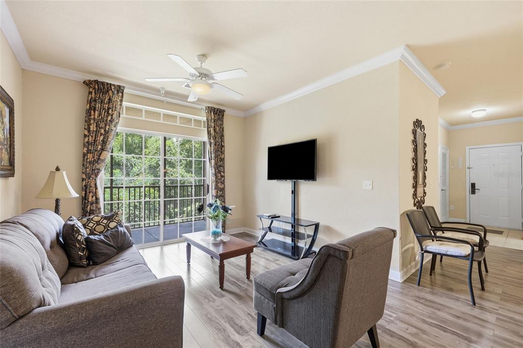 A living room features a grey sofa, an armchair, a television, and a sliding glass door — 8020 TUSCANY WAY UNIT 6206, DAVENPORT, FL