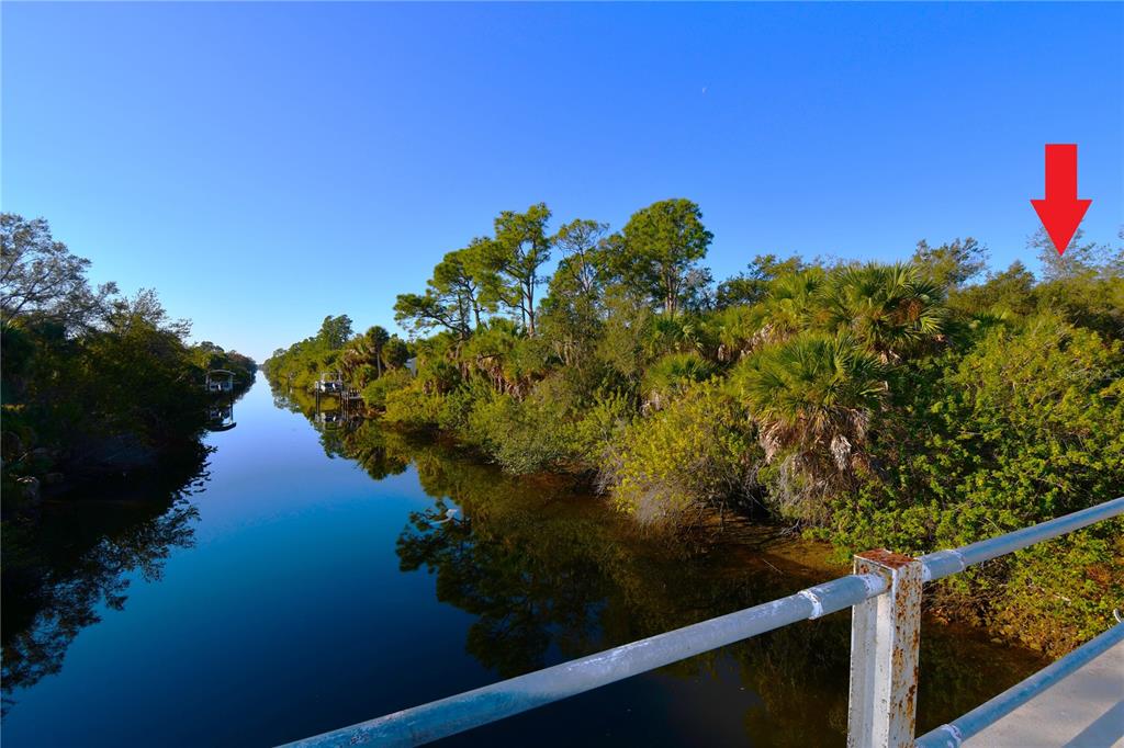 A view of a narrow canal lined with dense trees and vegetation under a clear sky — 17255 WINTERGARDEN AVENUE, PORT CHARLOTTE, FL