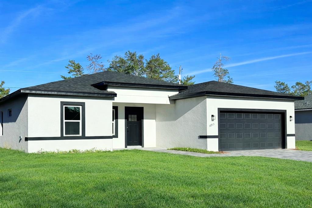 A single-story house with white stucco walls, black trim, and a two-car garage — 16915 SW 37TH TERRACE RD, OCALA, FL