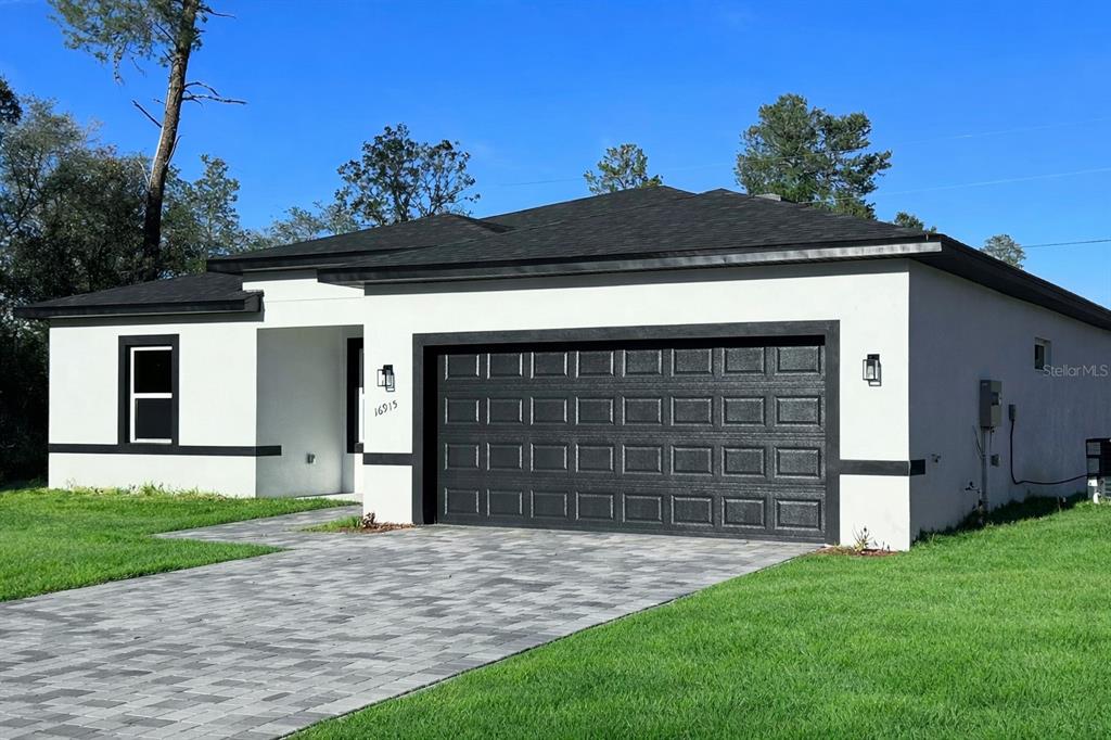 A single-story house with white stucco walls, a black garage door, and a paved driveway — 16915 SW 37TH TERRACE RD, OCALA, FL