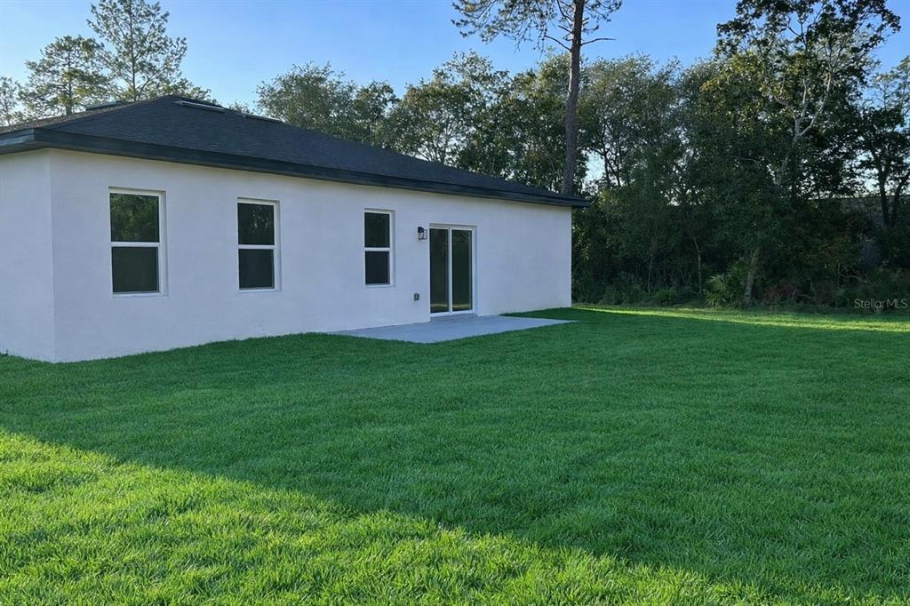The exterior rear view of a white house features a concrete patio and green lawn — 16915 SW 37TH TERRACE RD, OCALA, FL