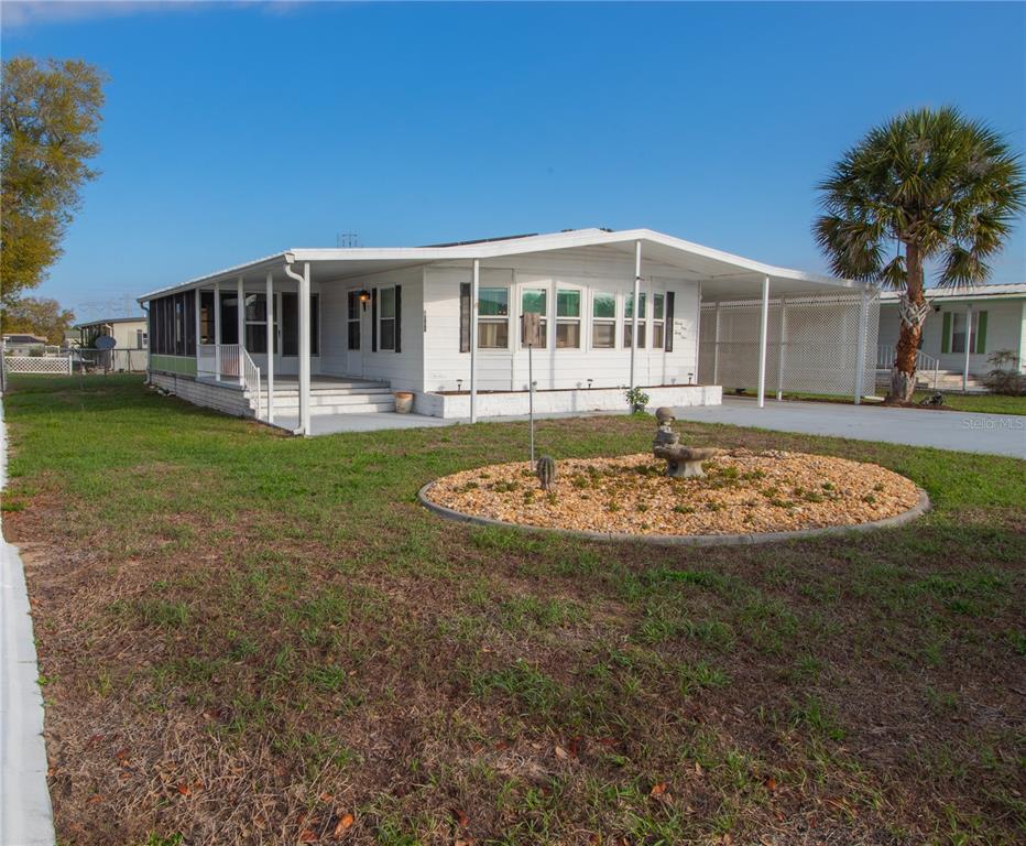 A white mobile home features a covered porch, a carport, and a circular gravel garden — 9141 SALISBURY DRIVE, BROOKSVILLE, FL