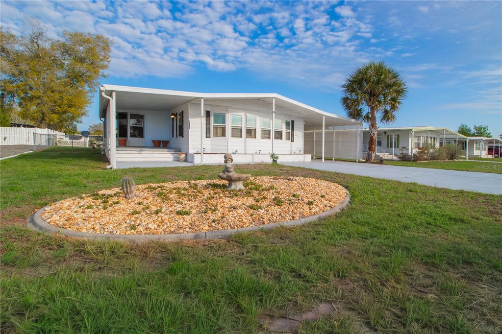 A white mobile home with a covered carport and a landscaped rock garden in front — 9141 SALISBURY DRIVE, BROOKSVILLE, FL