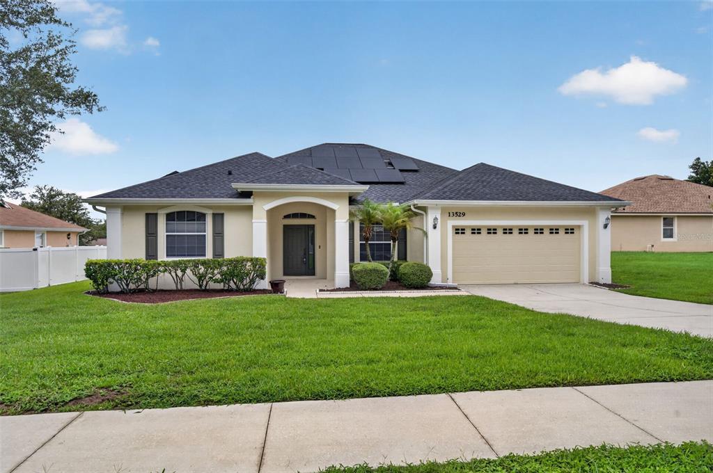 A single-story suburban house with a tan exterior, dark roof, and solar panels — 13529 VIA ROMA CIRCLE, CLERMONT, FL