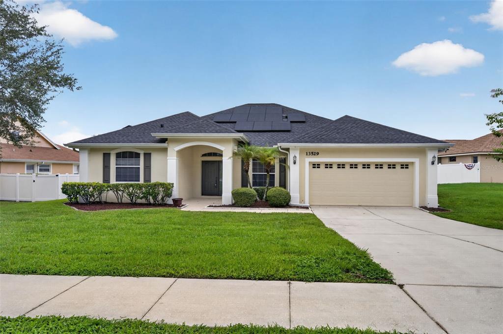 A single-story house with a beige exterior, a dark shingled roof, and a two-car garage — 13529 VIA ROMA CIRCLE, CLERMONT, FL
