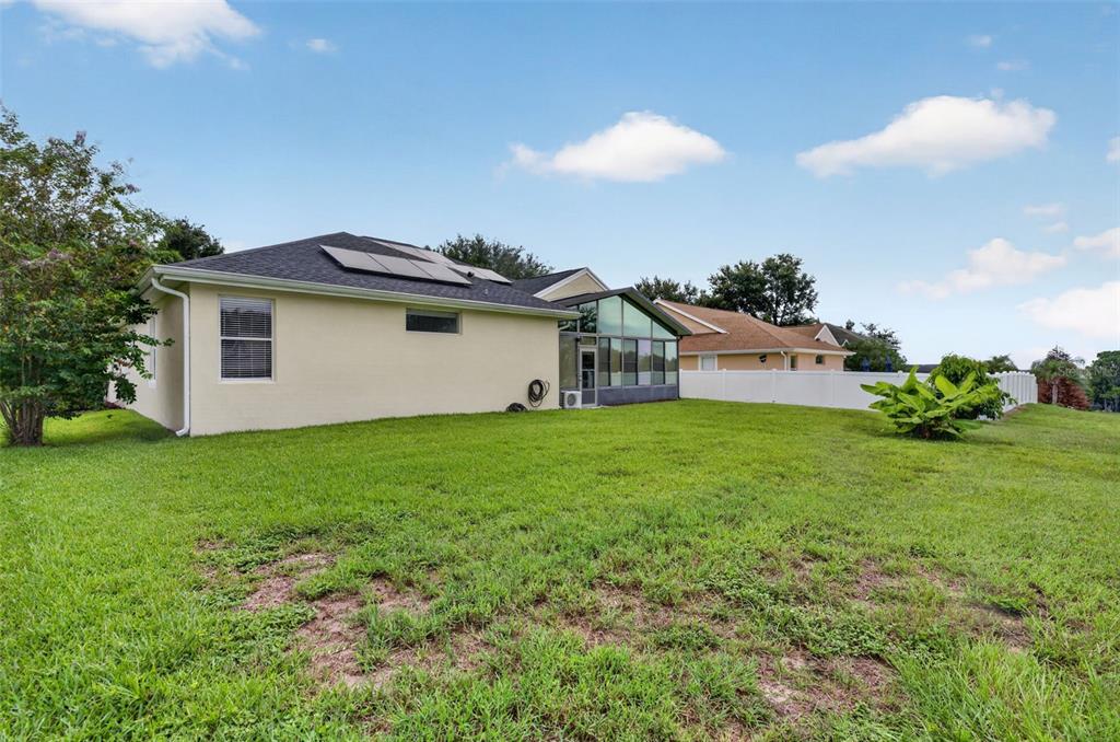 The exterior of a house with a sunroom, solar panels, and a large grassy backyard — 13529 VIA ROMA CIRCLE, CLERMONT, FL